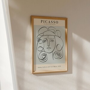 May include: A framed print of a black and white line drawing of a woman's face. The print is titled "PICASSO" and has the text "Anthera Galleria dell'arte Moderna, 1972" at the bottom.
