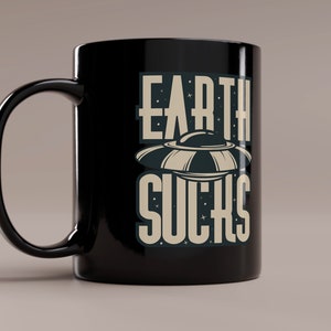 May include: Black ceramic mug with a white graphic of a UFO and the text "EARTH SUCKS".