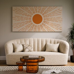 May include: A white, fluffy sofa with a tufted back and a sunburst design on the wall behind it. The sofa has three pillows, two white and one with a black and white pattern. There is a round glass coffee table in front of the sofa and a smaller round table next to it.