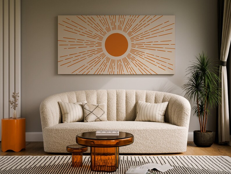 May include: A white, fluffy sofa with a tufted back and a sunburst design on the wall behind it. The sofa has three pillows, two white and one with a black and white pattern. There is a round glass coffee table in front of the sofa and a smaller round table next to it.