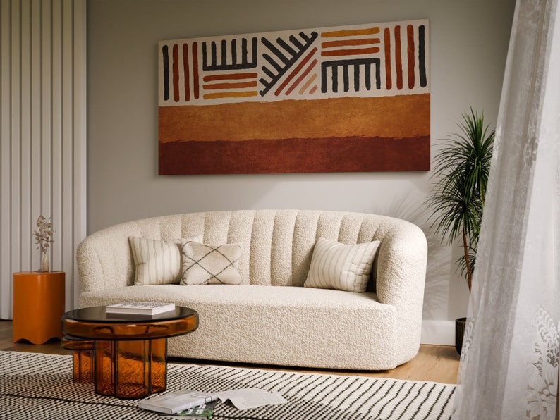 May include: A white, fluffy, curved sofa with pillows sits in a living room with a brown and orange abstract painting on the wall, a brown coffee table, and a small orange side table.