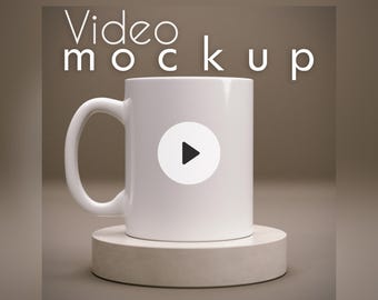 Könnte beinhalten: Ein schlichter weißer Keramikbecher mit geschwungenem Henkel steht auf einem runden, hellen Sockel. Der Becher zeigt einen weißen Kreis in der Mitte mit einem schwarzen Play-Button-Symbol. Der Text Video mockup steht in Weiß darüber.