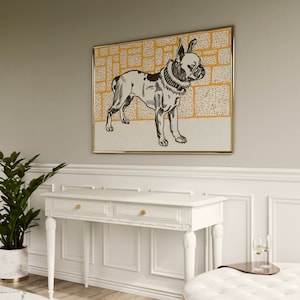 May include: A black and white illustration of a French Bulldog wearing a collar, set against a yellow and white patterned background. The illustration is framed in a gold frame and hangs on a light gray wall above a white console table.