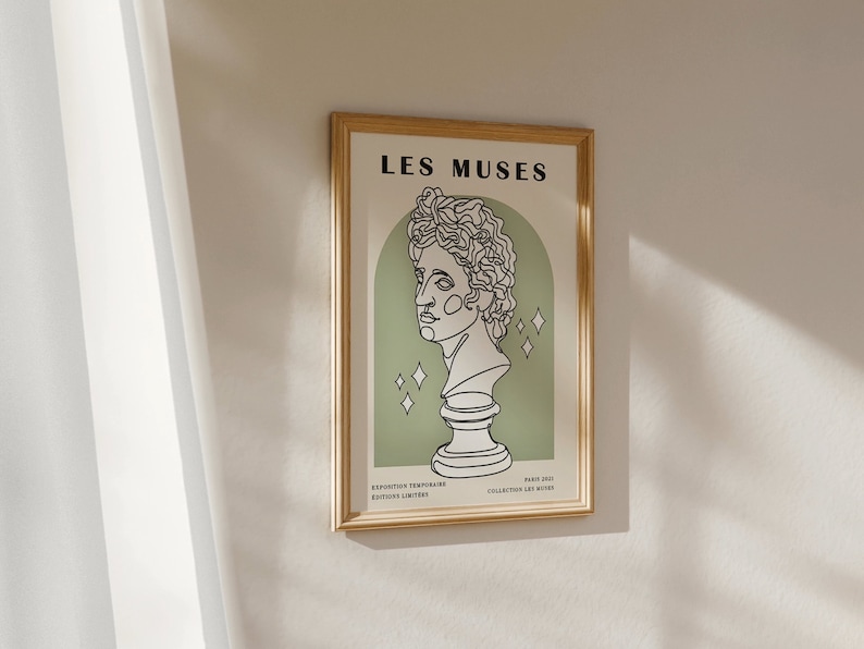 May include: A framed print with a gold frame and a white background. The print features a line drawing of a bust of a person with the text "LES MUSES" at the top. The text "EXPOSITION TEMPORELLE" and "GALERIE LIMITAIRE" are at the bottom left, and "PARIS 2023" and "COLLECTION LES MUSES" are at the bottom right.