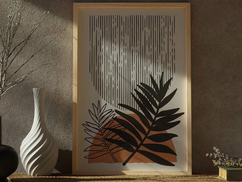 Op de afbeelding: Een ingelijst print met een minimalistisch ontwerp met zwarte en witte abstracte lijnen en een gestileerd zwart blad op een bruine achtergrond.
