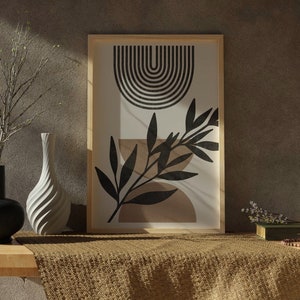 Op de afbeelding: Een ingelijste print met een geometrisch ontwerp in zwart en wit met een boog en een gestileerd blad. De print is op een witte achtergrond en is ingelijst in een naturel houten lijst. De print staat op een houten tafel met een bruin geweven kleed ervoor.