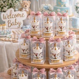 May include: A wooden stand displays carousel-themed baby shower favours. Each favour, in a clear box, features a white and gold carousel with pink ribbon. The name "Lujain" is printed on each base. A sign says "Welcome Baby".