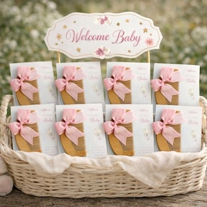 Puede incluir: Una cesta de mimbre contiene recuerdos de baby shower, incluyendo peines de madera adornados con lazos rosas. Un letrero que dice "Welcome Baby" está encima. También hay un oso de peluche y cajas de regalo.