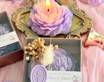 May include: A small, clear box with a purple rose candle inside. The box is decorated with dried flowers and a purple wax seal with a rose design. The box has a label that says "Thank you for celebrating Elena & Robert 09.12.2025".