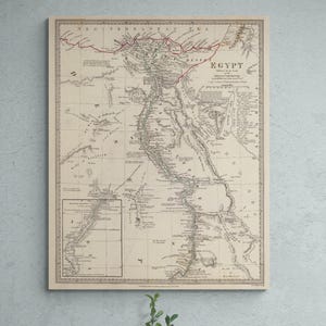 Może przedstawiać: Antyczna mapa Egiptu, oprawiona w jasną drewnianą ramę. Mapa zawiera szczegółowe informacje geograficzne, w tym Nil i okoliczne obszary. Mapa jest wydrukowana w odcieniach beżu i szarości, z tekstem wskazującym nazwę kraju.