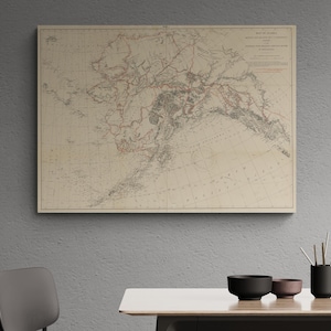 May include: A rectangular wall map of Alaska featuring detailed topographical lines, geographical markings, and printed text in the upper right corner. The map displays a beige background with black and red ink lines depicting terrain and borders.