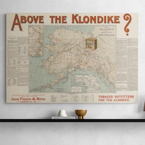 May include: A rectangular wall print titled Above the Klondike featuring a vintage map of Alaska with routes to the gold fields. The print includes text detailing John Finzer & Bros. tobacco outfitters, historical notes, and a large red question mark.