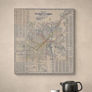 以下が含まれることがあります： Map of The City of Los Angelesというタイトルのヴィンテージ風の地図。ベージュの背景に黒、赤、黄色の道路線が描かれています。地図には文字と数字のグリッド枠があり、両サイドには詳細なテキストの列が配置されています。