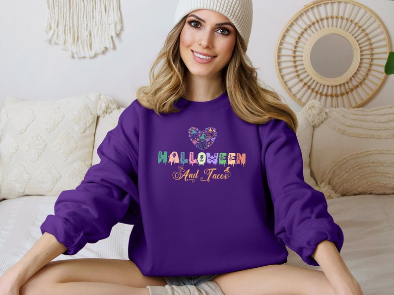 Funny I Love Halloween and Tacos Sweatshirt with a design in vibrant colors. Shirts are available in various colors.