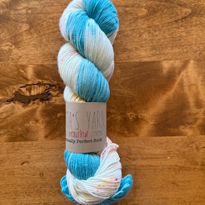 May include: A skein of yarn in a blue and white colorway with a label that reads "Mia's Yarn, A Beautiful Color, Really Perfect Sock."