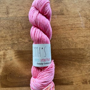 May include: A skein of pink yarn with a white label that reads "Emma's Crazy Beautiful Comfy Cotton DK".