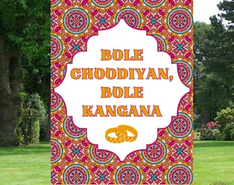 May include: A white sign with a pink and orange mandala pattern border. The sign has a white frame with a decorative border and the text "BOLE CHOODIYAN, BOLE KANGANA" in orange. There are two gold rings in the center of the sign.