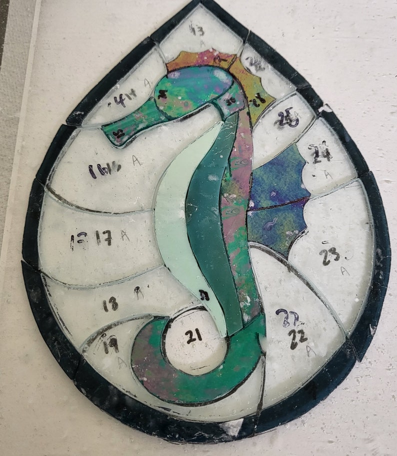 May include: A stained glass seahorse design with numbered pieces of glass. The seahorse is green, blue, and purple with a yellow and orange mane.