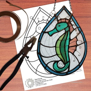 May include: A stained glass pattern for a seahorse, with a teal, green, and pink color scheme. The pattern is 6.75 inches by 9.75 inches and is 100% scale. The pattern includes instructions for using glass paint and overlay.