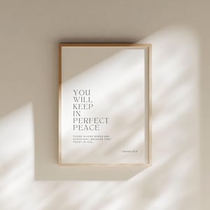 May include: A framed print with the text "YOU WILL KEEP IN PERFECT PEACE" in a minimalist style. The print also includes the text "THOSE WHOSE MINDS ARE STEADFAST, BECAUSE THEY TRUST IN YOU" and "ISAIAH 26:3". The frame is a light wood color.