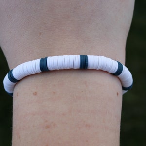May include: White and dark blue beaded bracelet. The bracelet is made of round beads with a white base and a dark blue stripe around the middle of each bead.
