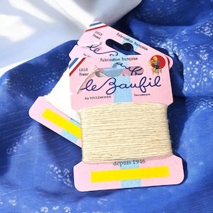 May include: Two spools of natural coloured thread on pink and white packaging with the text "le Baufil" and "Fabrication française" in blue and black lettering. The packaging also includes the text "Ets TOULEMONDE" and "Successeurs" in black lettering. The bottom of the packaging has a yellow label with the text "depuis 1946" in black lettering.