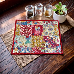 May include: A square quilted fabric mat featuring a patchwork design of various colourful patterns, including elephants, birds, and floral motifs in shades of red, blue, yellow, and green, finished with a solid red fabric border trim.