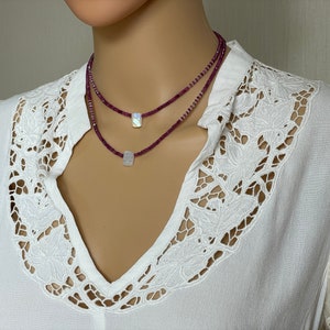 May include: A layered necklace with two strands of small, dark pink beads and two rectangular iridescent white stones.