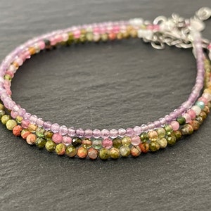 Peut inclure: Un bracelet multi-rangs composé de petites perles rondes dans des tons de rose, vert et violet. Les perles sont enfilées sur une chaîne argentée.