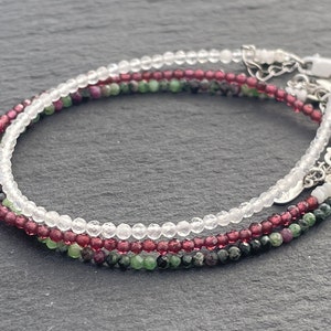 May include: Three layered bracelets with small beads. The top layer is white, the middle layer is red, and the bottom layer is green.