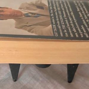 Puede incluir: Un libro de bolsillo con una columna vertebral de color canela y una cubierta negra. La cubierta presenta una foto de un hombre con traje y corbata. El texto de la cubierta dice "Gay Talese" y "The Kingdom and the Power".