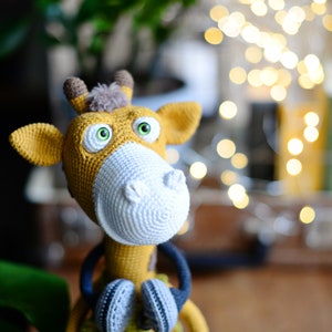 May include: A crocheted giraffe toy with large green eyes, a white crocheted nose, and yellow and brown fur. The giraffe is wearing a blue and gray crocheted scarf.