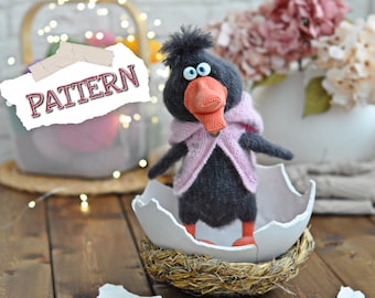 May include: A crocheted black bird with a pink scarf and orange beak sits in a broken white egg shell. The egg shell is in a woven nest. The bird has large blue eyes. The background is a white brick wall with a wicker basket and pink flowers.