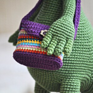 May include: A green crocheted stuffed animal with a purple and multi-colored striped crocheted purse.