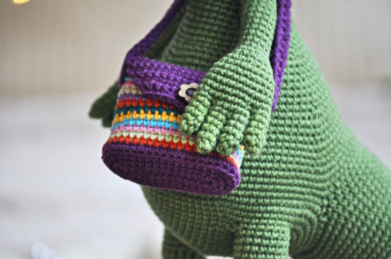 May include: A green crocheted stuffed animal with a purple and multi-colored striped crocheted purse.