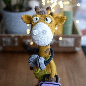 May include: A crocheted giraffe toy wearing headphones and holding a purple and yellow boombox. The giraffe has brown spots and green clothing.