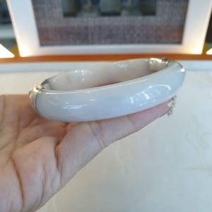 Peut inclure: Un bracelet jonc en jade clair et lisse. Le bracelet est de forme arrondie et polie. Le jade a une teinte subtile et crémeuse. Une petite chaîne en argent est attachée au bracelet.