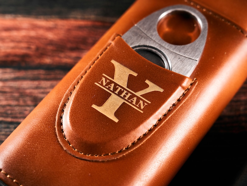 May include: A brown leather cigar case with a built-in cutter. The case has a personalized monogram with the name "Nathan" and the letter "Y".