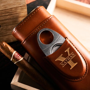 May include: A brown leather cigar case with a built-in cutter and a personalized inscription that reads "Nathan Y".