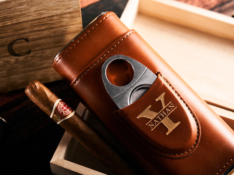 May include: A brown leather cigar case with a built-in cutter and a personalized inscription that reads "Nathan Y".