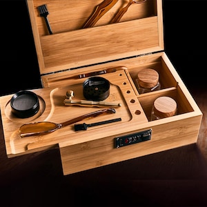 May include: A bamboo box with multiple compartments, including a tray with a screen, a pipe, and a grinder. The box also contains small glass jars with wooden lids and a combination lock.