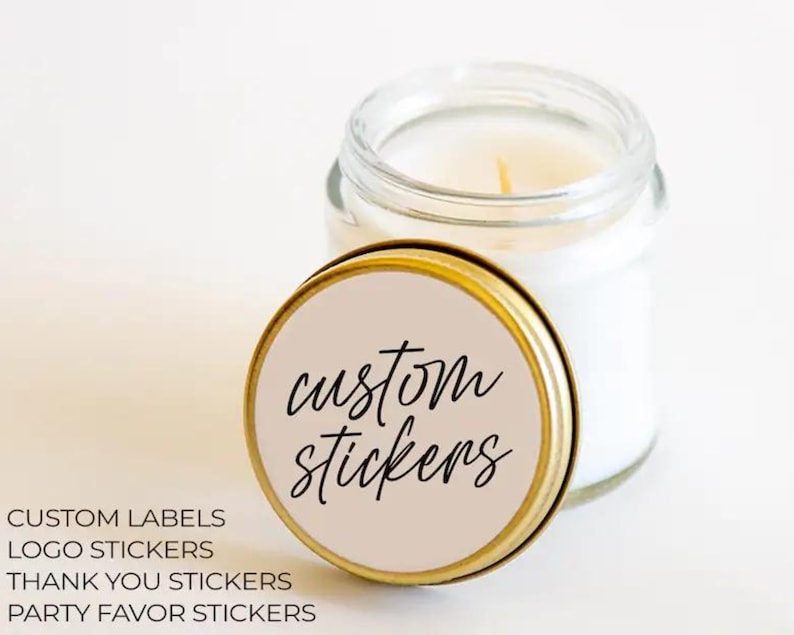 May include: A small glass jar candle with a gold lid. The lid features the words "custom stickers" in a handwritten font on a light tan background. Below the jar are the words "CUSTOM LABELS, LOGO STICKERS, THANK YOU STICKERS, PARTY FAVOR STICKERS."