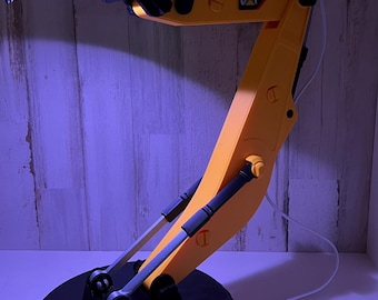 May include: A yellow and black desk lamp shaped like a construction excavator with a black base and a white switch on the cord. The lamp has the word "CAT" printed on the arm.