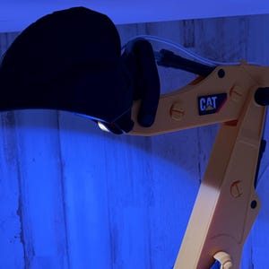 May include: Close-up of a yellow toy excavator arm with a black bucket. The arm has a CAT logo on it.