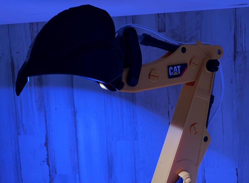 May include: Close-up of a yellow toy excavator arm with a black bucket. The arm has a CAT logo on it.