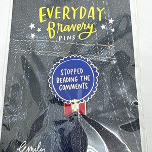 May include: A pin with the text "STOPPED READING THE COMMENTS" in white on a blue background, with a scalloped edge. The pin is part of the "EVERYDAY Bravery PINS" collection. A red and white bow is at the bottom.