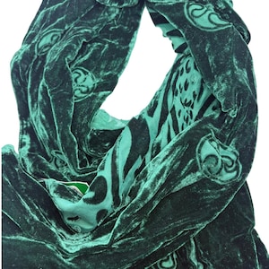 May include: Emerald green velvet scarf with a swirling pattern and a contrasting animal print design. The scarf is draped, showcasing its texture and the intricate details of the fabric. The scarf is a fashion accessory.