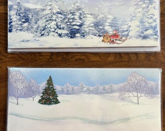 May include: Two Christmas-themed greeting cards. The top card depicts a snowy forest scene with a person on a sled pulled by reindeer. The bottom card shows a decorated Christmas tree in a snowy landscape with bare trees.