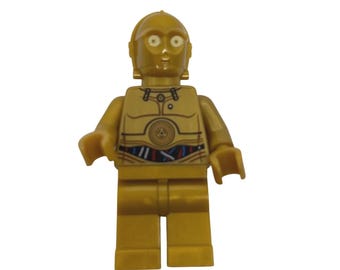 May include: A gold-coloured plastic toy figure representing a humanoid robot with a rounded head, circular eyes, and a torso featuring printed mechanical details including wires in red, blue, and black across the waist area and a circular chest plate.