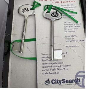 May include: Two silver keys with green ribbon, featuring the CitySearch logo and website address. The keys are on a printed invitation for the launch of CitySearch 2.0 in San Francisco, October 30, 1996.